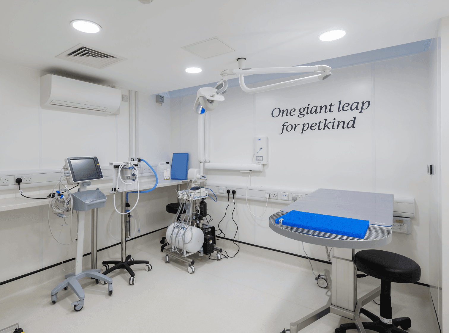 A modern veterinary clinic room with medical equipment and the text "One giant leap for petkind" on the wall.